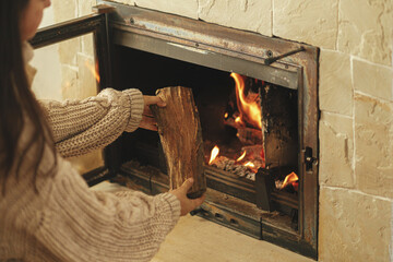 Heating house in winter with wood burning stove. Woman throwing firewood into burning fireplace in...