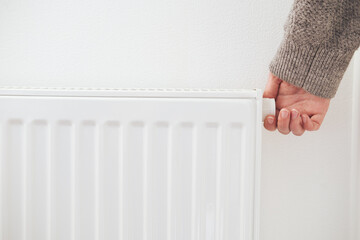 Hand turning down thermostat of a central heating radiator. Energy saving, cold winter season,...