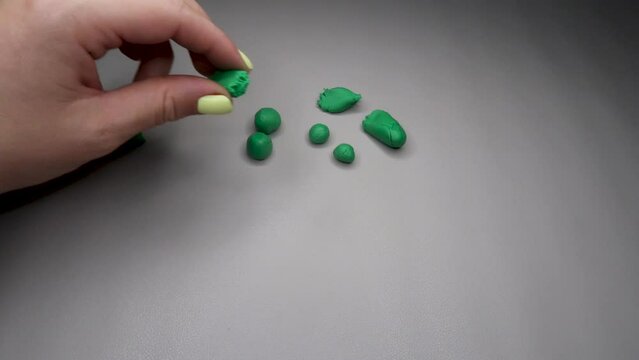A quick time-lapse of a woman with a yellow manicure sculpts two frogs from plasticine on a light background