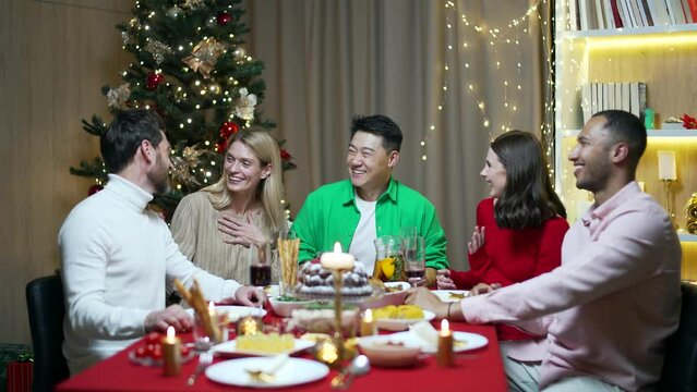 Festive Christmas eve dinner, various visiting friends sitting at table eating resting and laughing, celebrating new year together group of men and women. Group young people having fun enjoy in house