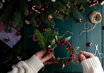 Close-up female hands decorate a Christmas wreath on a green wooden table in a Christmas decor