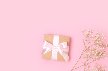Present with a tied ribbon and branch of gypsophila flower on a pink pastel background. Minimal festive concept with copyspace.