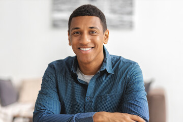 Smiling successful African American man smiling and looking at the camera sitting at workplace in modern office. Young positive male confident entrepreneur or freelancer