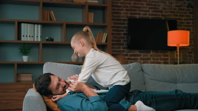 Caucasian man babysitter dad lying on sofa playing with loving child daughter tickling play children game having fun enjoy pastime together playful childhood at home on holiday laughing happy family
