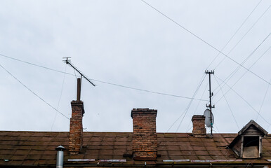 Roof of old house with brick chimneys and electrical wires on gray sky background