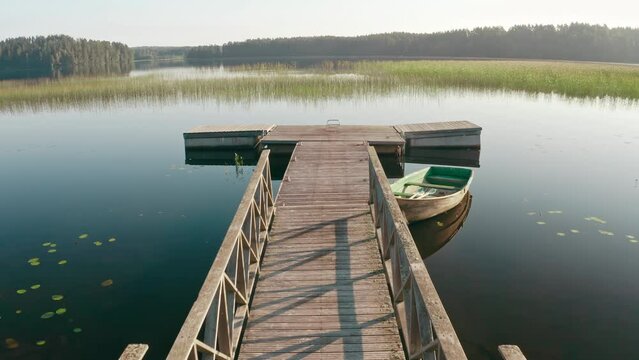 Drone flies over wooden old boat moored at the pier on a large lake among the forest and trees at dawn on a summer day