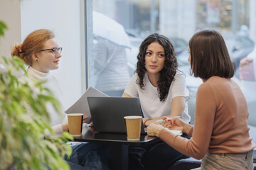 three female friends or colleagues are working and doing brainstorming. students or business partners in coworking create a project. young successful women entrepreneurs and designers. small business