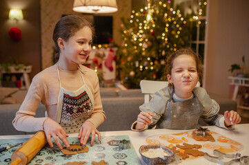 Fototapeta premium Girls have fun and joyfully prepare Christmas cookies at home in the kitchen