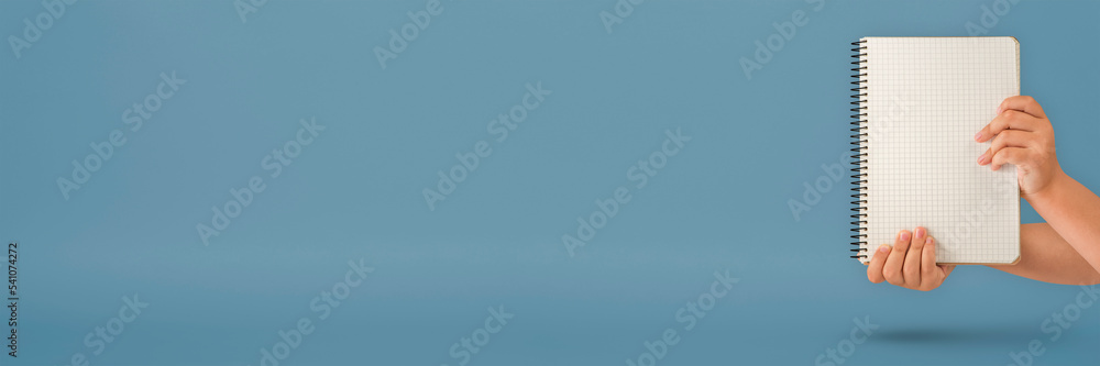 Wall mural Notepad in hand. Blank notepad in the hands on a blue background. Hands hold a book without text. The girl is holding a book with an empty cover.