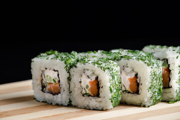 Uramaki sushi roll on wooden tray on black background. Popular Asian dish.