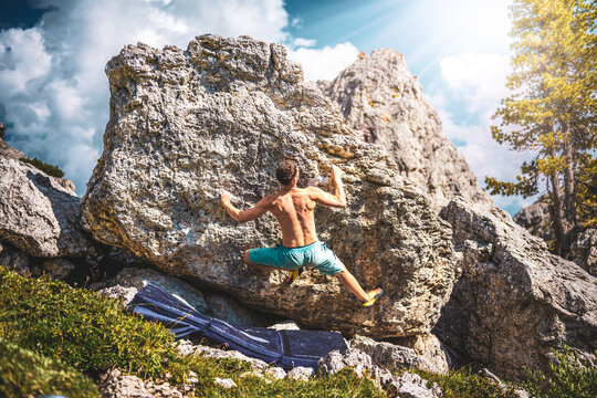 Sporty shirtless man climbs on boulder problem in the afternoon. Falzarego pass, Dolomites, South Tirol, Italy, Europe.