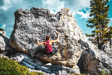 Sporty woman climbs on boulder problem in the afternoon. Falzarego pass, Dolomites, South Tirol,...