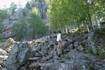 Girl tourist climbs the stones in the mountains. Forest, summer, day.