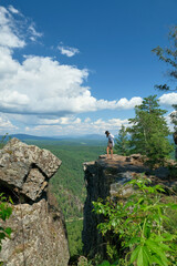 Landscape, mountains, valley. A girl is standing on a rock. Summer, greenery, blue sky and clouds.