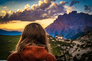 Sporty woman in outdoor jacket watches beautiful sunset mountain scenery at Rifugio Passo...