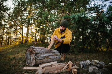 A survivalist chops wood for a nighttime bonfire.