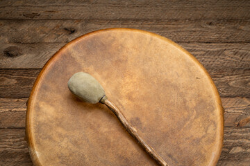 handmade, native American style, shaman frame drum covered by goat skin with a beater on a rustic wood
