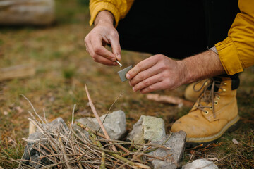 Survival in the wild. A bearded man lights a fire near a makeshift shelter made of pine branches.