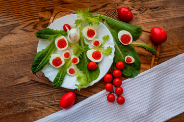 Naklejka na ściany i meble background of red caviar on dark wooden surface. edible egg rabbit figurine for decorating dishes easter dish decorated with red painted Easter eggs, cherry tomatoes and lettuce leaves