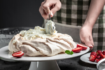 delicious homemade Pavlova cake with fresh strawberries and whipped cream. Female baker decorating delicious meringue cake, top view. place for text