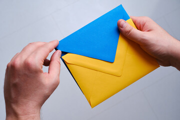 A man holds a yellow and blue paper envelope in his hand. New mail, message. Postal service. The...