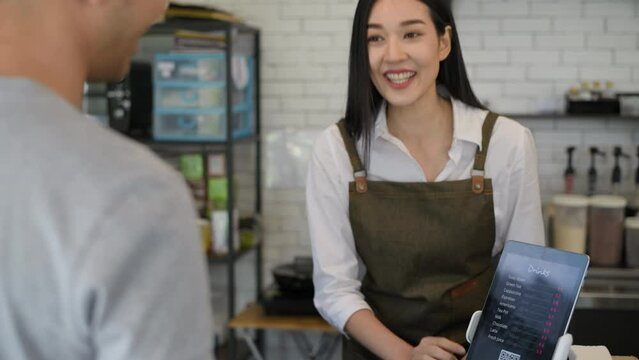 Coffee shop concept of 4k Resolution. Asian female staff are introducing menus to customers and paying by tablet.