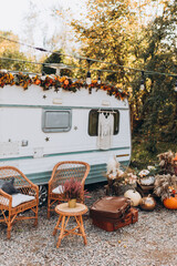 Wooden chairs and table placed outside cozy retro caravan on autumn day in countryside. Camping life concept - obrazy, fototapety, plakaty