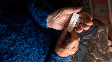 Close-up of caucasian grandma hand holding a buffer dropper for seft detection of coronavirus at...