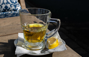 Close-up transparent cup of chamomile tea on the wooden table outdoors, a lemon wedge  and a tea spoon next to it