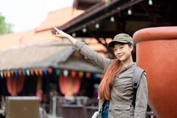 Young asian woman traveler with mask and backpack pointing finger on famous tourist attractions in...