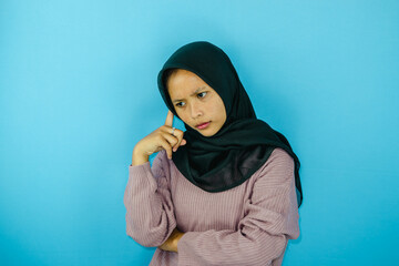 Portrait of thinking young Asian woman wearing hijab isolated on blue background