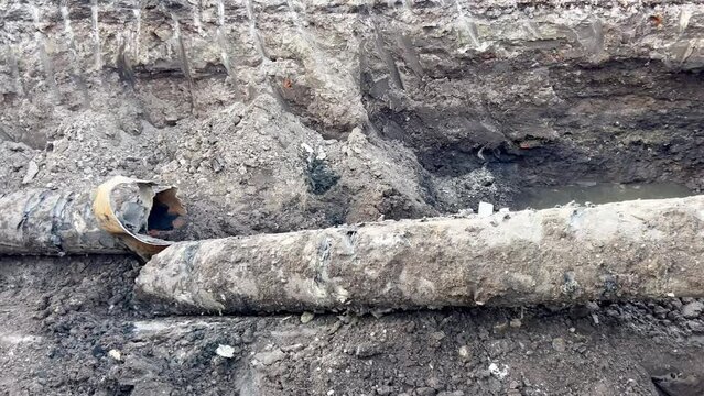 Old cracked concrete sewer pipe. Replacement of old worn sewer pipes underground. Excavation of drains, replacement of old sewage equipment. A funnel from an aerial bomb in the ground, a cracked pipe