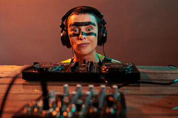 Young performer acting funky looking at mixer, being focused on control buttons at dj turntables...