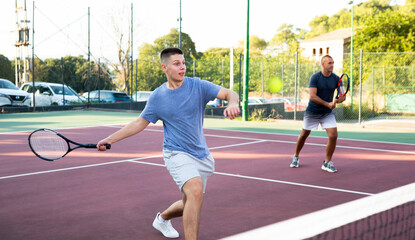 Obraz premium Sports active man during friendly doubles couple match. Two men playing together tennis outdoor