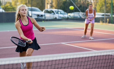 Obraz premium Sports active woman during friendly doubles couple match. Two women playing together tennis outdoors