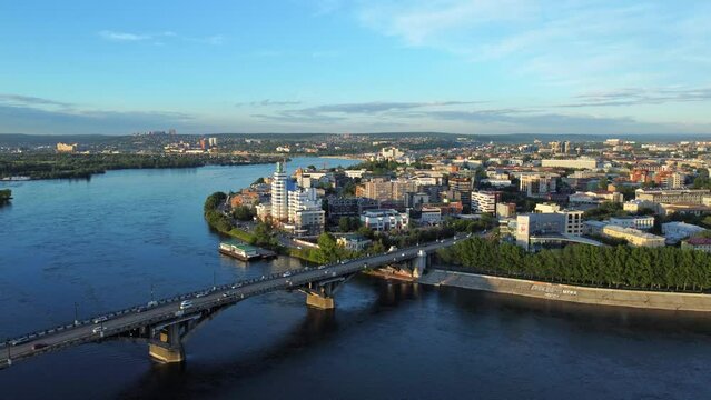 4k Beautiful top view of Irkutsk city on summer day irrl. Aerial pic of cars driving along bridge over blue river in modern town with buildings and infrastructure outdoors. Amazing drone view of