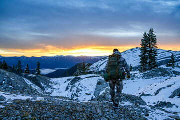 Male hunter walks along a rocky mountain ridge in Wyoming, on a hunting trip during sunrise. Snow on mountains