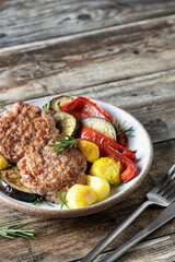 Fried cutlets and salad of grilled vegetables potatoes zucchini red pepper rosemary on wooden background with cutlery. Dinner menu with text space