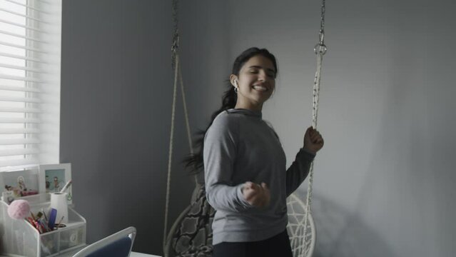Teenage girl wearing earbuds dancing and singing to music in bedroom / Lehi, Utah, United States