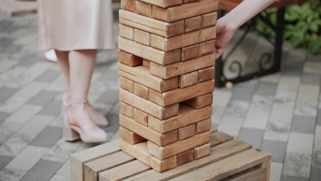 Two unrecognizable women are playing wooden jenga outside.