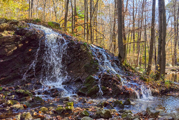 A small waterfall spilling over rocks with yellow and orange autumn leaves on trees