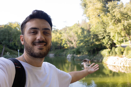 Young smiling man casual clothes taking selfie with lake. He invites to nature.