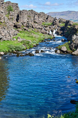 Fototapeta na wymiar A view of the blue clear water of Drekkingarhylur (Drowning Pool) as it sits alongside the rock walls of Almannagja Fault in Thingvellir National Park, Iceland.