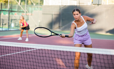 Young beautiful sportswoman in white t-shirt and shorts playing tennis on open summer court. Racket sport training outdoors