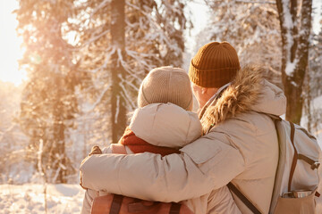 Back view of mature couple embracing in winter forest lit by sunlight, copy space