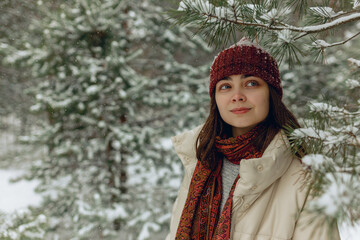 Dreamy woman in warm clothes standing under snowy tree in winter forest and looking away 