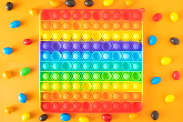 Push Bubble Fidget Toy Pop It on colorful background and candy. Trendy rainbow anti-stress sensory toy popit for popping bubbles. Flat lay, top view.