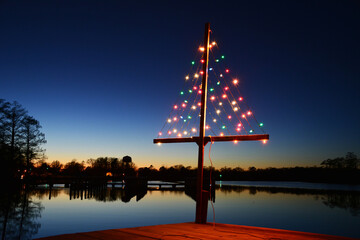 Christmas lights in the shape of a tree placed on the end of a dock at sunset.
