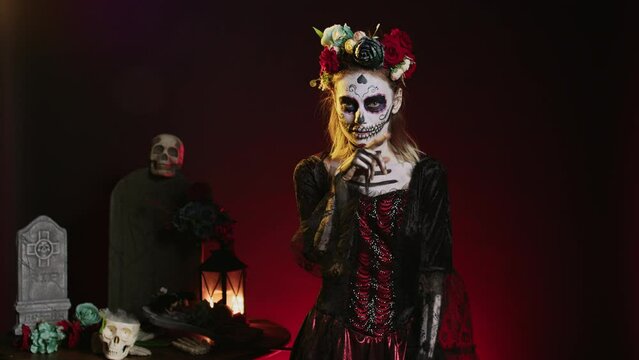 Creepy female model doing hush gesture to keep secret, wearing santa muerte costume and showing slience mute and secrecy sign with finger over lips. Holy dios de los muertos holiday.