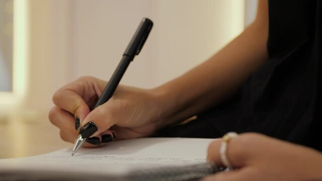 Hand of young woman with black nails writes in notebook, does homework. Concept of lifestyle and work at home. Female writer hand, closeup